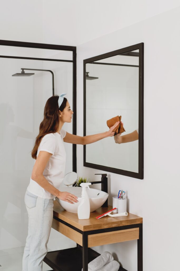 Woman cleaning mirror in bathroom.